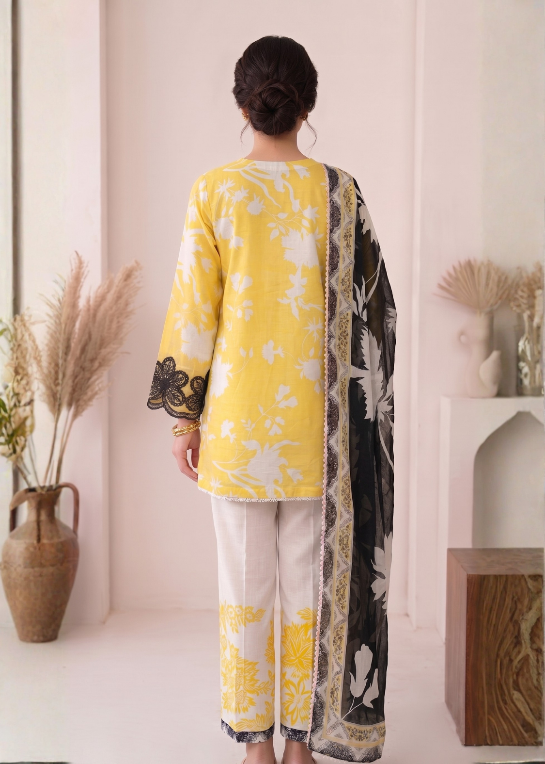 Person wearing a yellow and white floral outfit with a black and white patterned dupatta in a minimalistic setting.